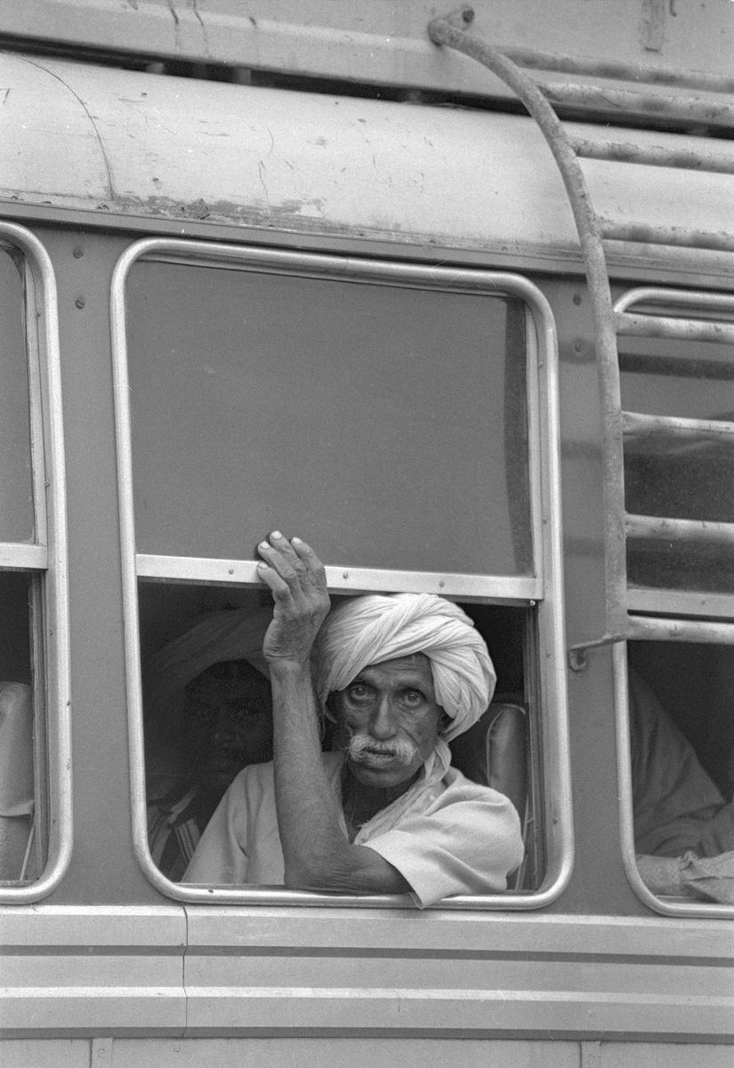 An old man in a turban leaning on the window of a bus, looking straight at the camera.